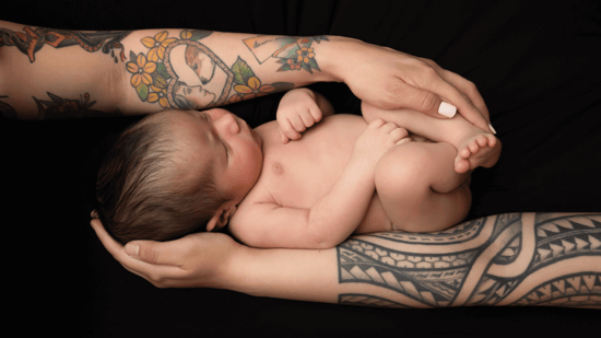 two tattooed arms of mothers hold newborn son against black background