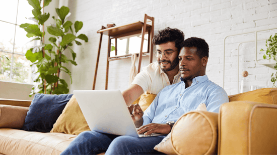 gay male couple at home sitting on couch looking at laptop