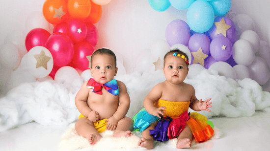 boy girl twins wearing rainbow outfits sitting in front of rainbow balloon arch