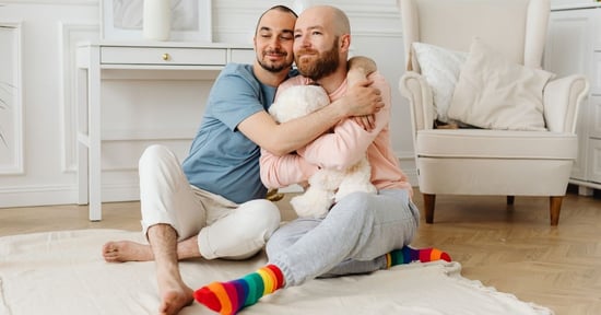 gay dads to be surrogacy sitting on floor hugging stuffed animal