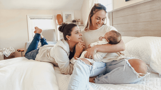 two moms with baby sitting on bed LGBTQ parents 
