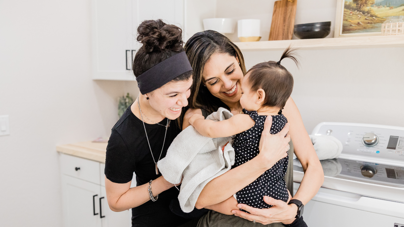 smiling-lgbtq-moms-with-baby-standing-in-kitchen